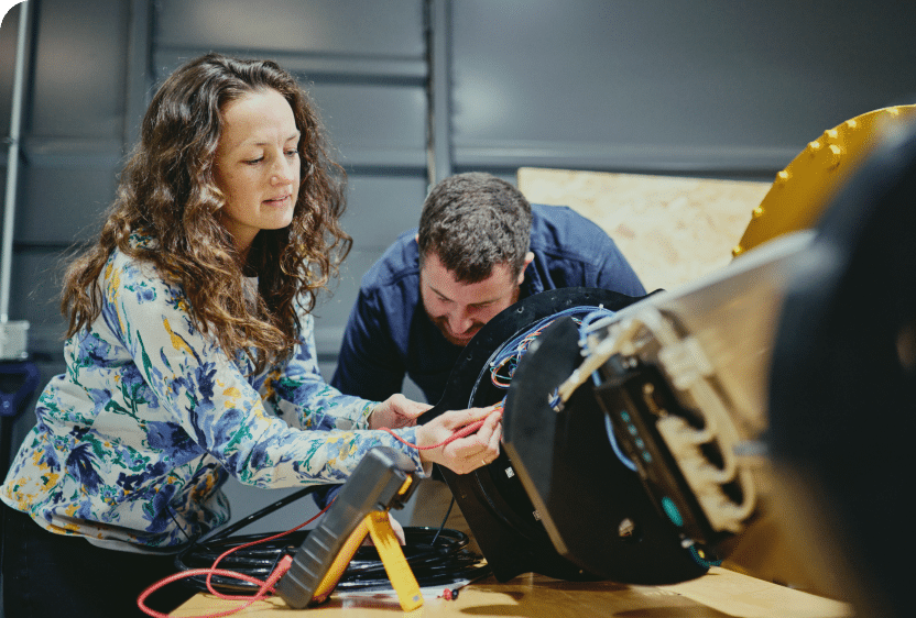 A man and a woman working on a device with electrical cords